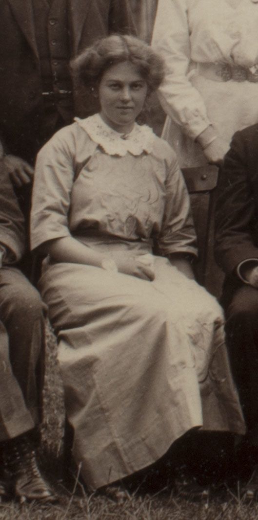 Formal photograph of woman seated outside. She has her hands in her lap.