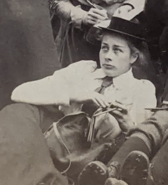 Black and white photograph of a woman seated outside. She is reclining and not facing the camera. She is holding a notebook and pencil.