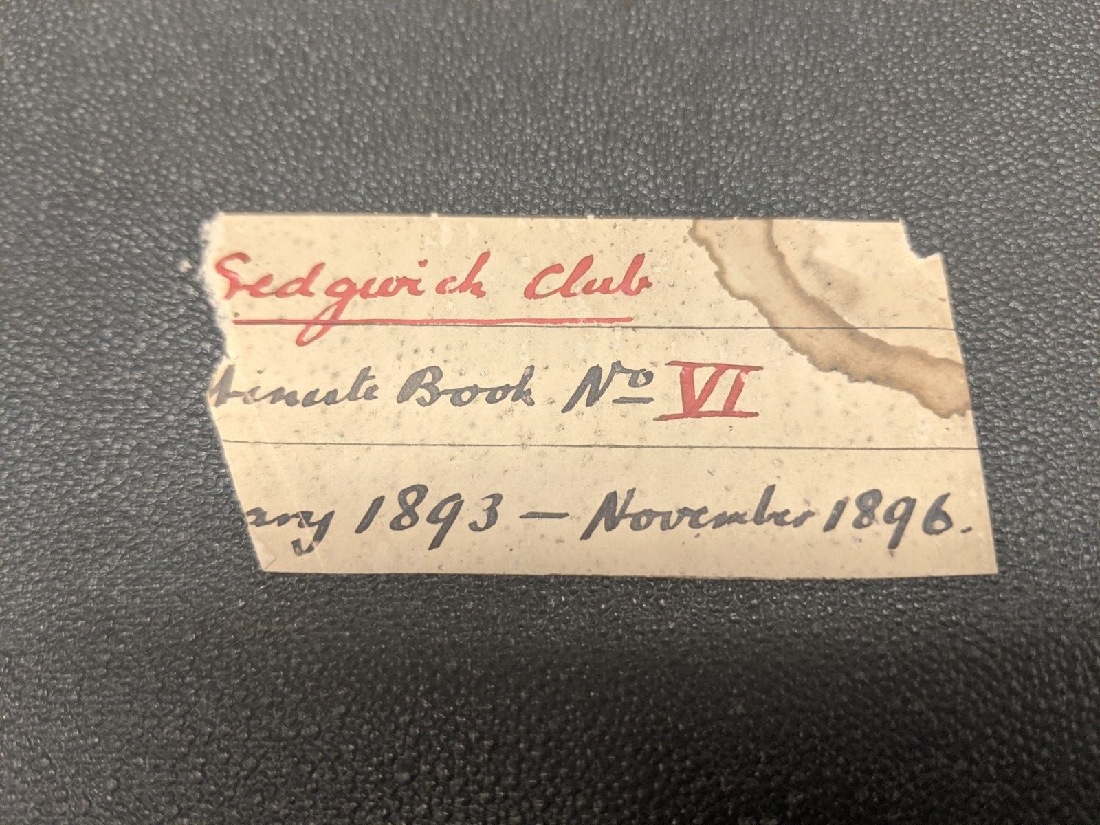 Torn label attached to the front of a note book. It has a coffee stain in the top right hand corner.